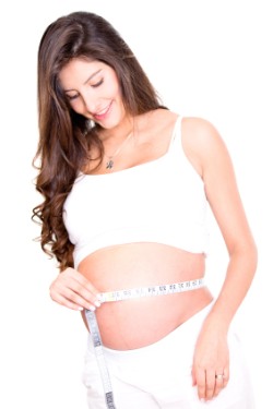 A pregnant women is smiling in this picture while looking at her belly. 
