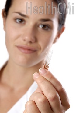 Woman holding up copper handle acupuncture needles for display. 